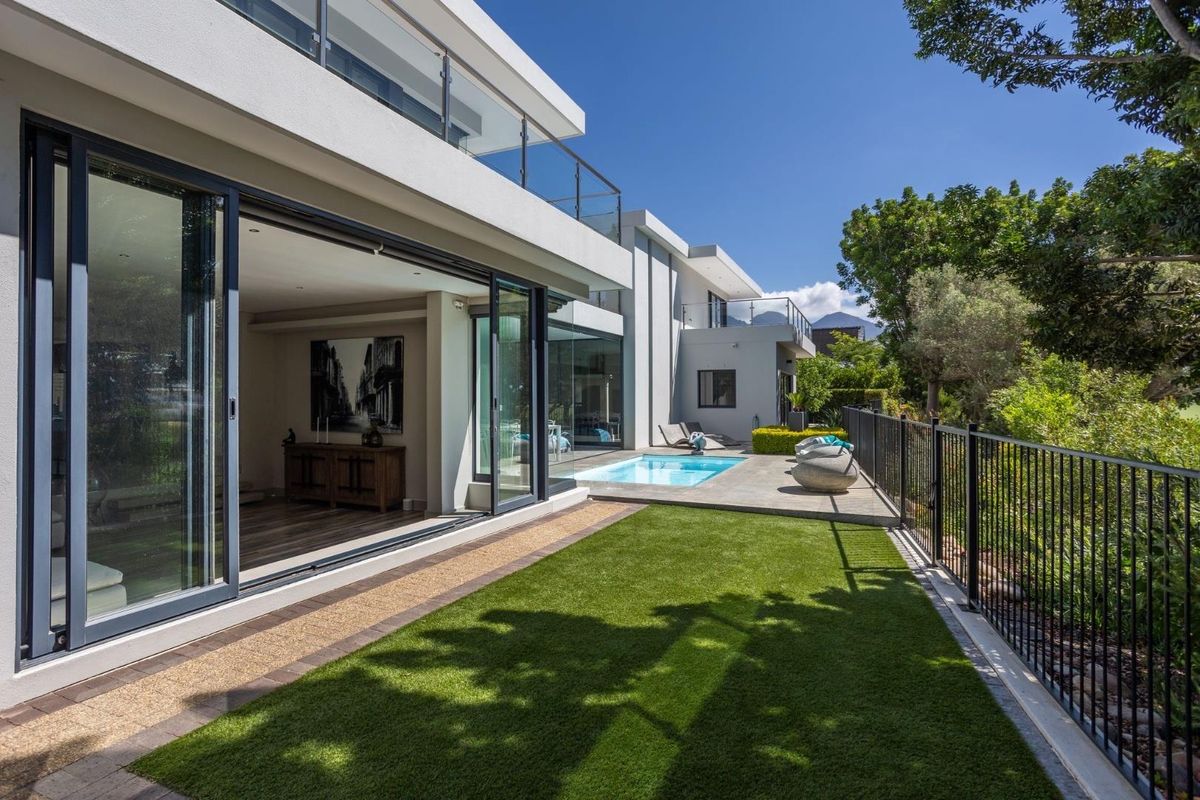 Modern rear exterior featuring a swimming pool, paved patio area, artificial lawn, and large sliding glass doors connecting to the interior living space.