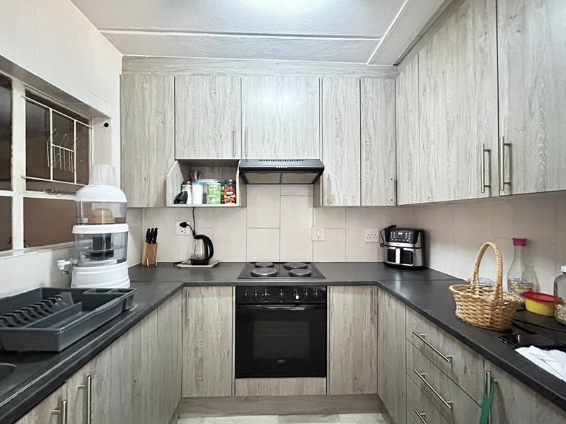 A functional U-shaped kitchen featuring light wood-grain cabinetry, dark countertops, a built-in oven, and an electric hob with an integrated extractor fan.