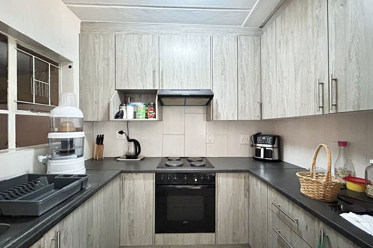 A functional U-shaped kitchen featuring light wood-grain cabinetry, dark countertops, a built-in oven, and an electric hob with an integrated extractor fan.