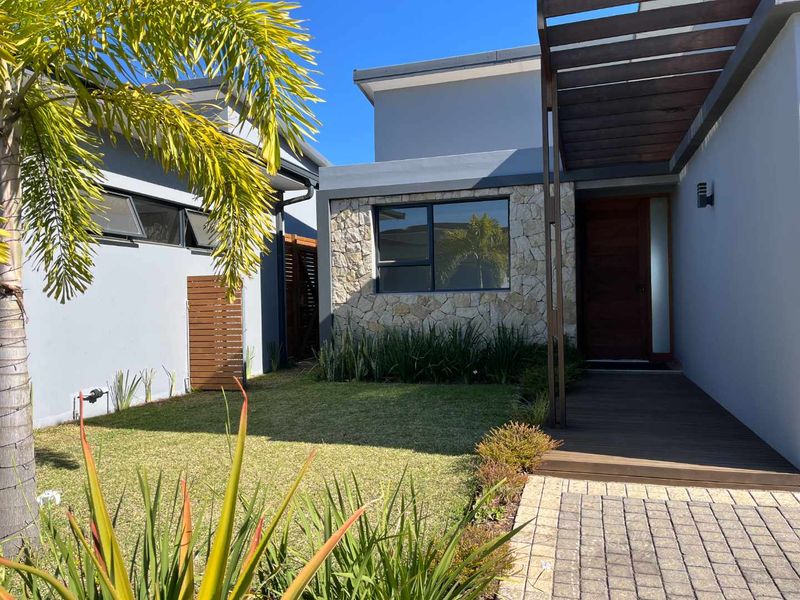 Modern townhouse entrance featuring stone cladding, a timber pergola over a wooden deck, and a well-maintained front garden with paved access.