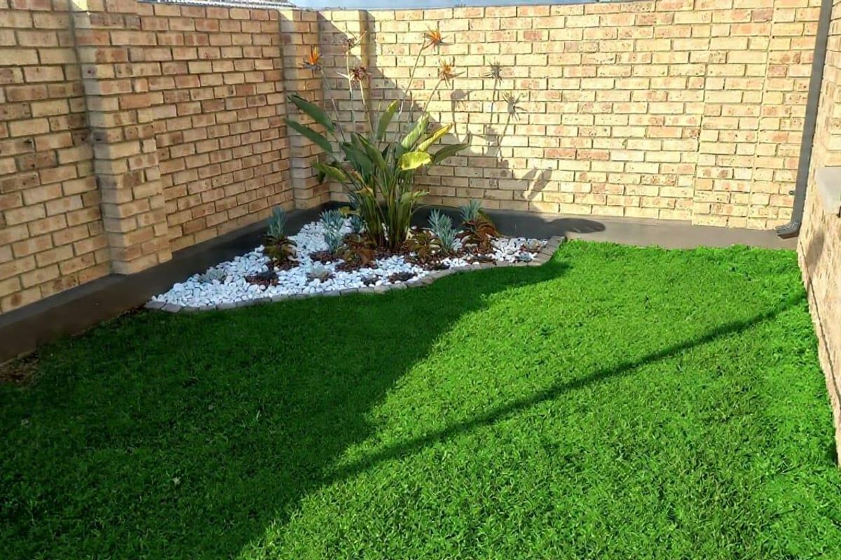 A neat rear garden area featuring a face brick boundary wall, artificial lawn, and a landscaped corner garden bed.