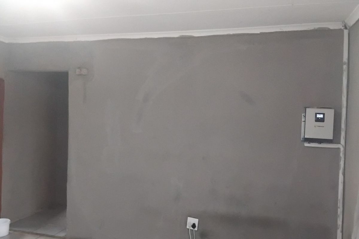 An interior room featuring unfinished plastered walls and a wall-mounted solar inverter unit, presenting a blank canvas for final interior finishes.