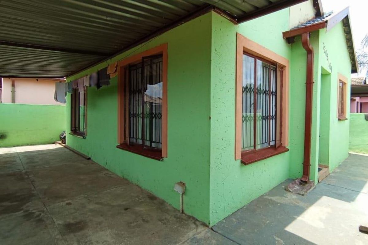 Side view of the house featuring a covered carport area, concrete paving, and security bars on the windows.