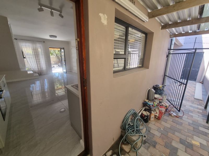 A covered outdoor patio area with paved flooring and security gate, providing access to the interior living space.
