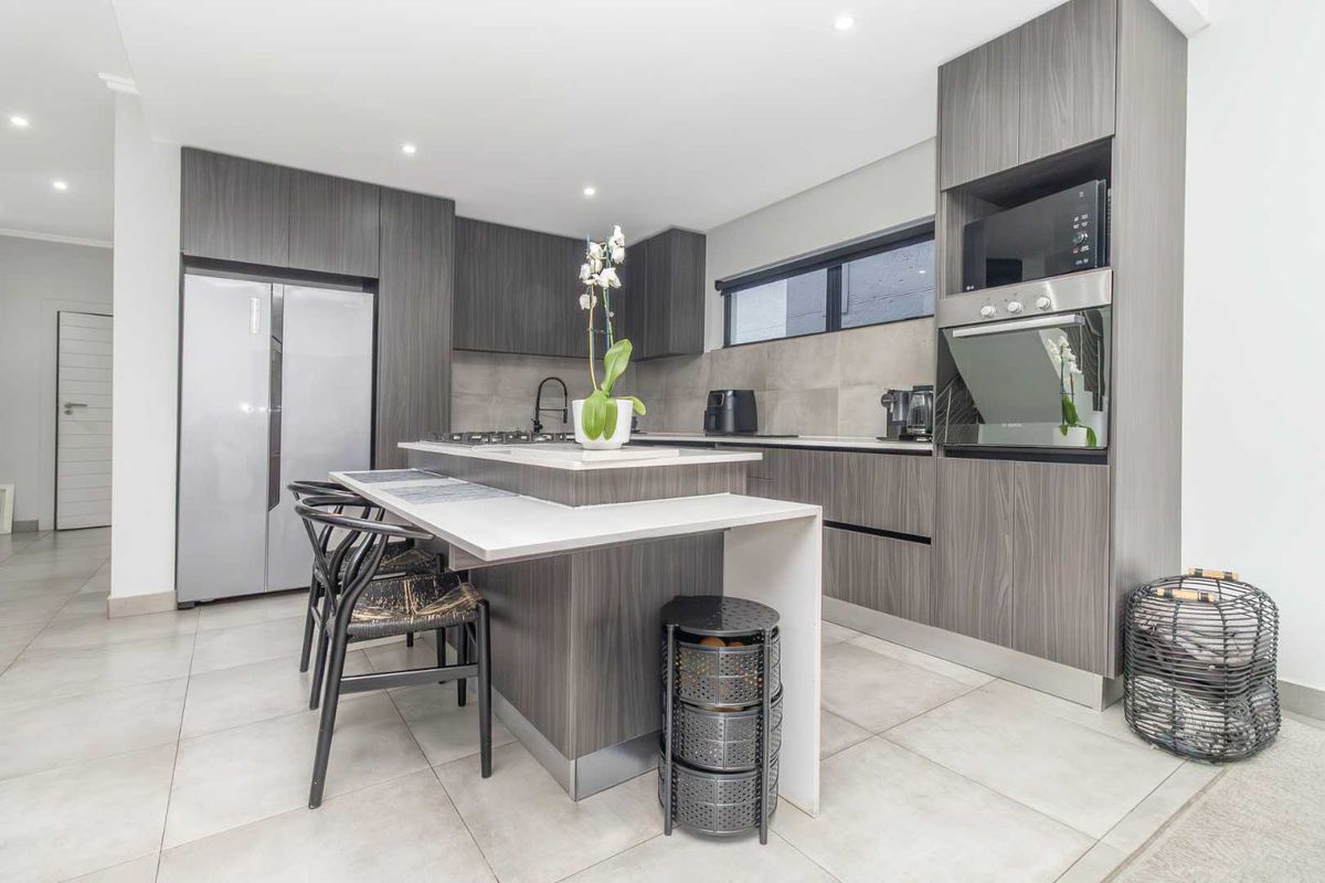 Modern kitchen featuring dark wood-grain cabinetry, stone countertops, a central island with breakfast bar, and integrated stainless steel oven and microwave.