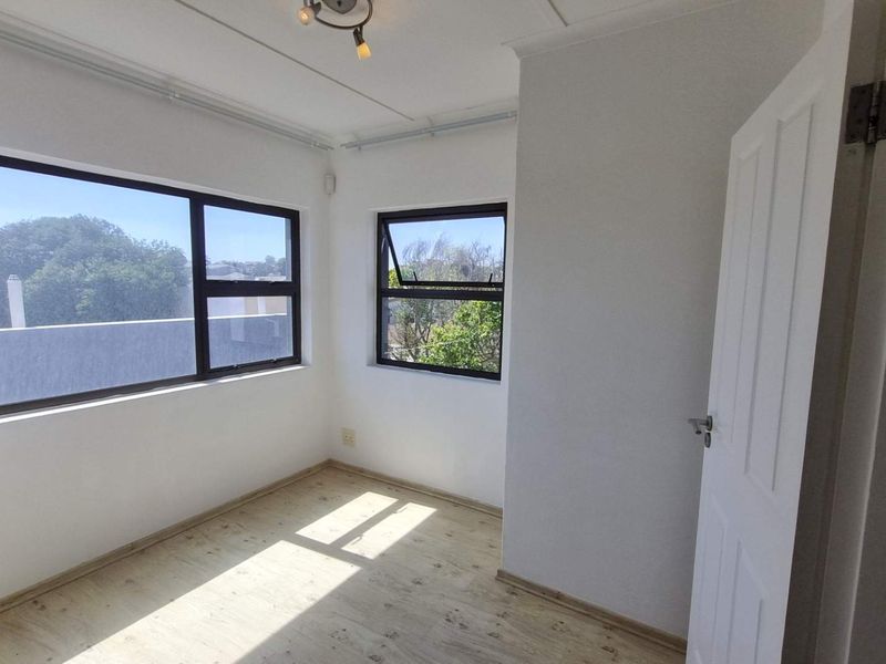 A bright, empty bedroom featuring modern laminate flooring, neutral walls, and large aluminium-framed windows providing ample natural light.
