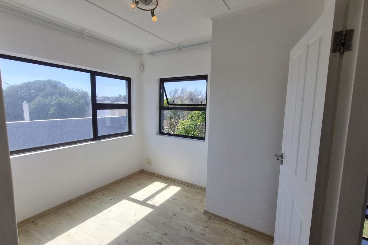 A bright, empty bedroom featuring modern laminate flooring, neutral walls, and large aluminium-framed windows providing ample natural light.