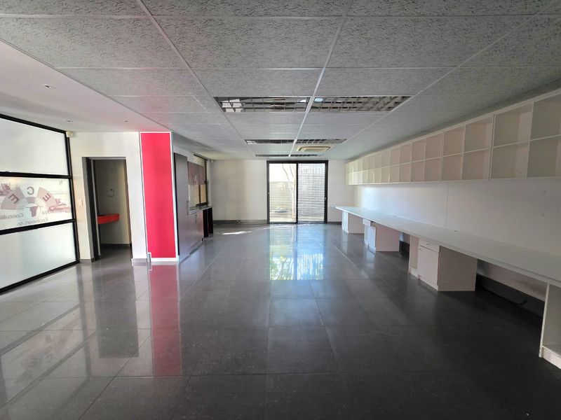 Spacious open-plan office area featuring tiled flooring, extensive built-in desk space, overhead cabinetry, and a sliding glass door leading to an outdoor area.