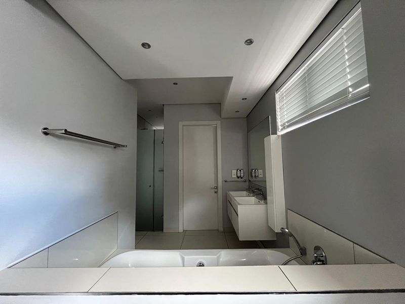 Modern bathroom featuring a built-in bathtub, double wall-mounted vanity, tiled flooring, and recessed lighting with clean, neutral finishes.