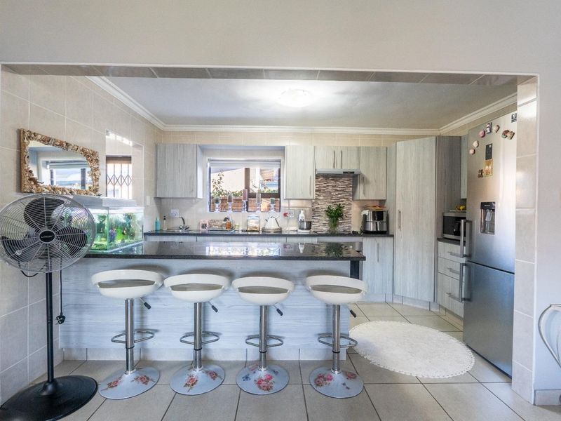 A functional kitchen featuring light wood-grain cabinetry, dark granite countertops, a breakfast bar, and tiled flooring, offering a clean and practical cooking space.