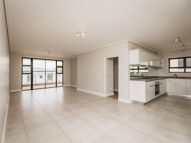 Spacious open-plan living area featuring modern tiled floors, a sleek kitchen with integrated appliances, and large sliding doors leading to a balcony.