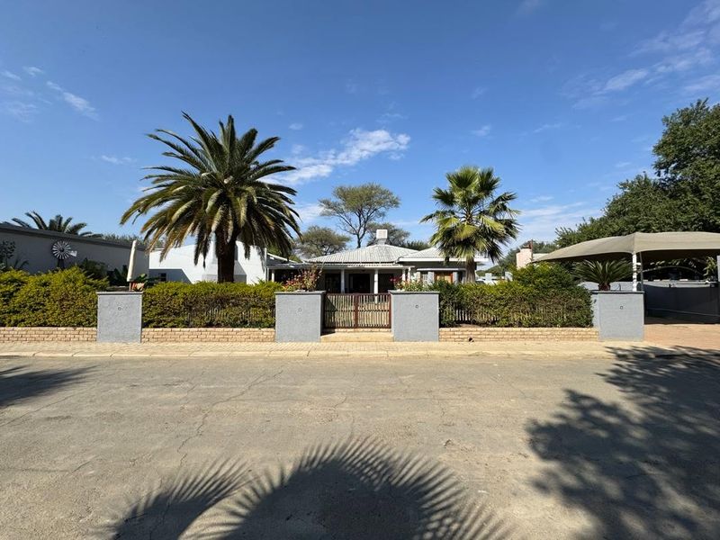 Front elevation of the guest house featuring a secure gated entrance, brick boundary walls, and a shaded carport area.