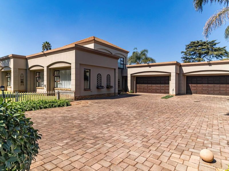 Spacious front exterior view featuring a large paved driveway, double garage, and well-maintained plastered facade under a clear blue sky.