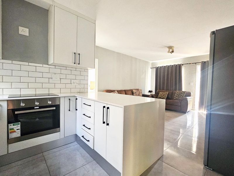 Modern open-plan kitchen featuring white cabinetry, stone countertops, and a subway tile backsplash, seamlessly flowing into the adjacent living area with tiled floors.