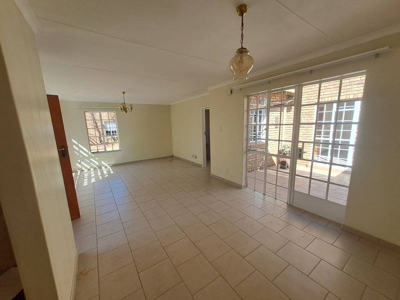 Spacious, light-filled living area featuring neutral tiled flooring, classic coved ceilings, and direct access to an outdoor patio through glass-paned french doors.