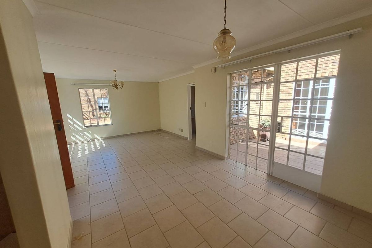 Spacious, light-filled living area featuring neutral tiled flooring, classic coved ceilings, and direct access to an outdoor patio through glass-paned french doors.