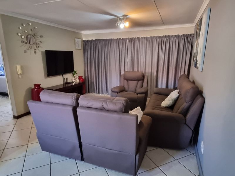 A comfortable living room featuring tiled flooring and ceiling coving, with an adjacent view into a bedroom area.
