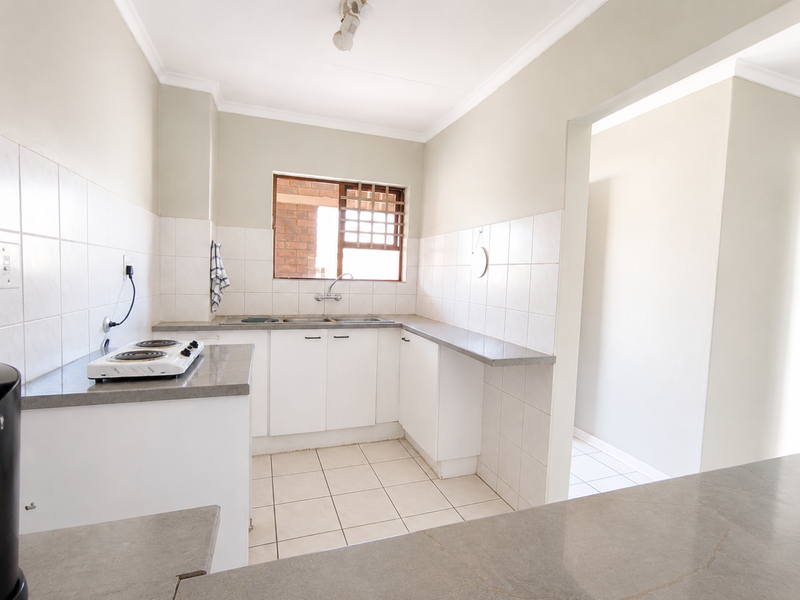 A functional, empty kitchen featuring white cabinetry, stone countertops, tiled backsplash, and ceramic flooring, offering a clean canvas for modern updates.