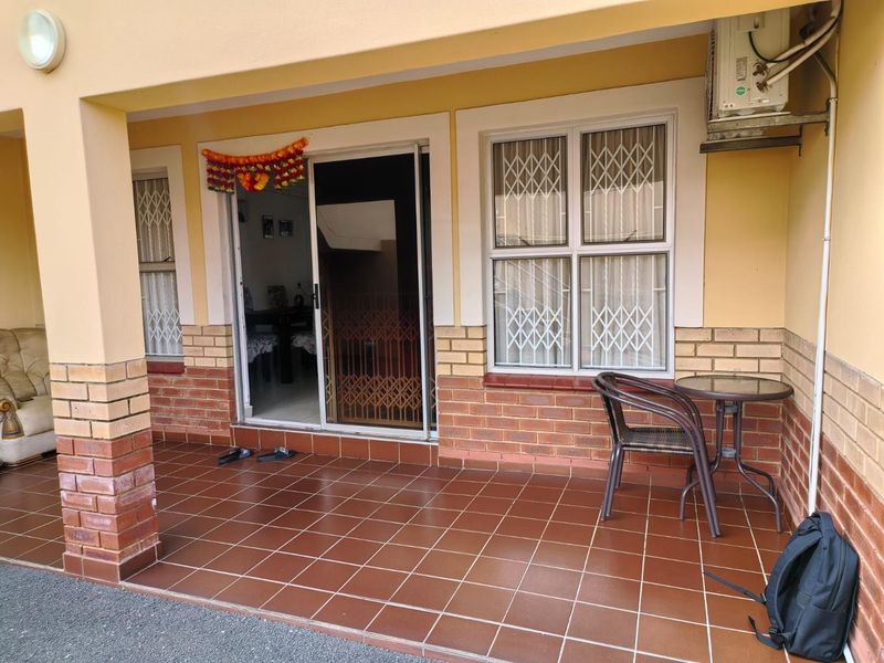 A covered patio area featuring tiled flooring, brick accents, and security gates, providing a functional outdoor space for relaxation.