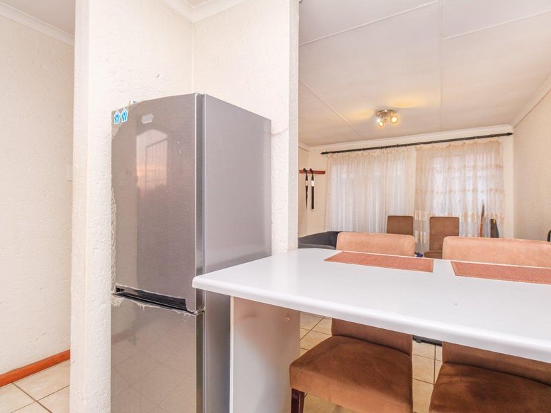 Open plan living and dining area featuring tiled flooring and a breakfast bar, showing signs of wear on the wall finishes.