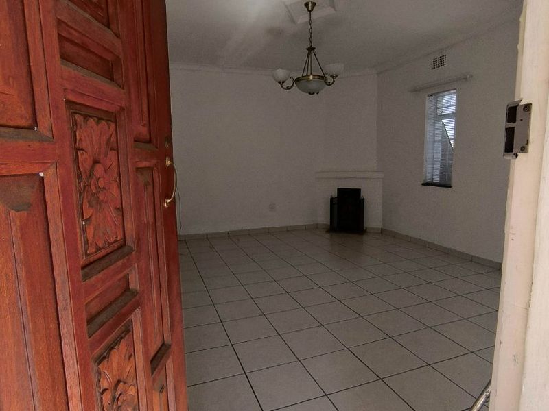 An empty living room featuring tiled flooring, a fireplace, and a decorative wooden entrance door, offering a blank canvas for interior design.