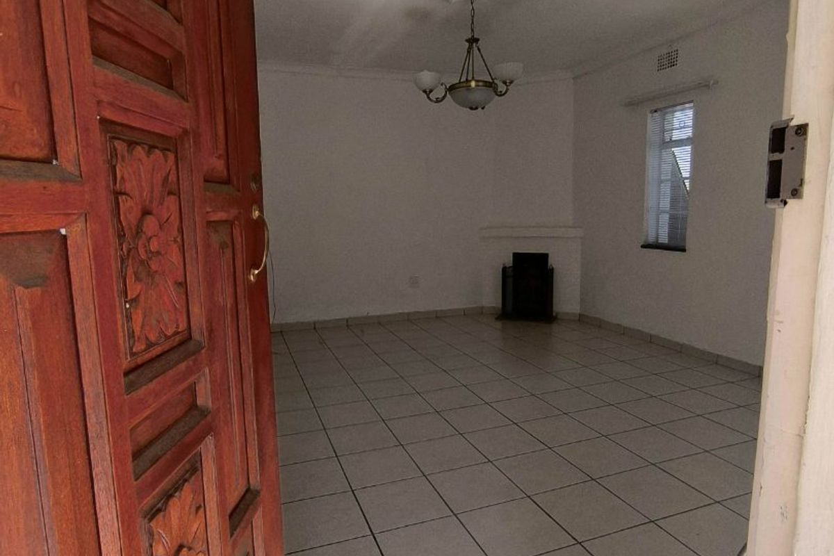 An empty living room featuring tiled flooring, a fireplace, and a decorative wooden entrance door, offering a blank canvas for interior design.