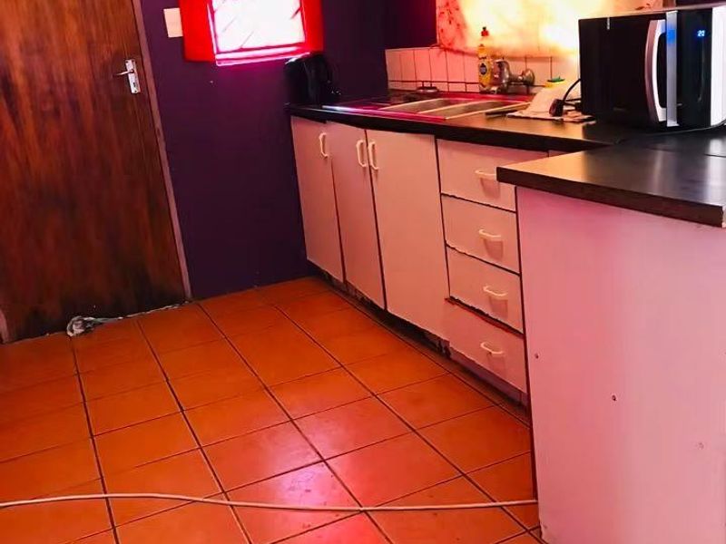 A dated kitchen featuring built-in cabinetry, laminate countertops, a stainless steel sink, and tiled flooring, requiring cosmetic updates to modernize the space.