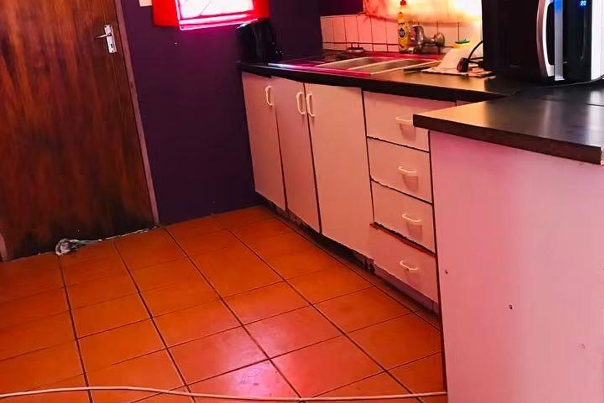 A dated kitchen featuring built-in cabinetry, laminate countertops, a stainless steel sink, and tiled flooring, requiring cosmetic updates to modernize the space.