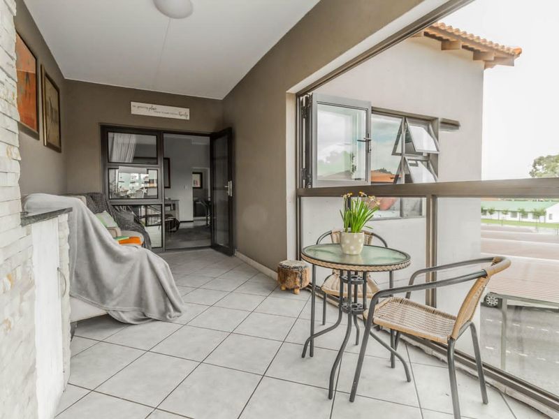 A covered balcony featuring tiled flooring, a glass balustrade, and a stone-clad feature wall, offering an inviting outdoor space.