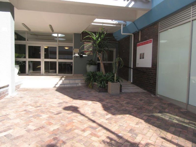 A paved entrance area featuring a brick facade, glass doors, and an accessibility ramp leading to the building entrance.