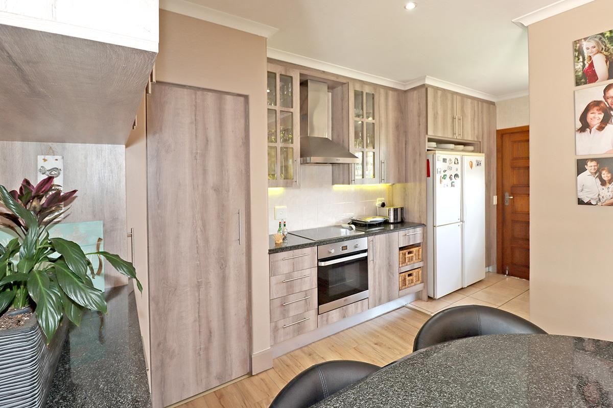 Modern kitchen featuring wood-look cabinetry, granite countertops, built-in oven, glass cooktop, and stainless steel extractor fan.