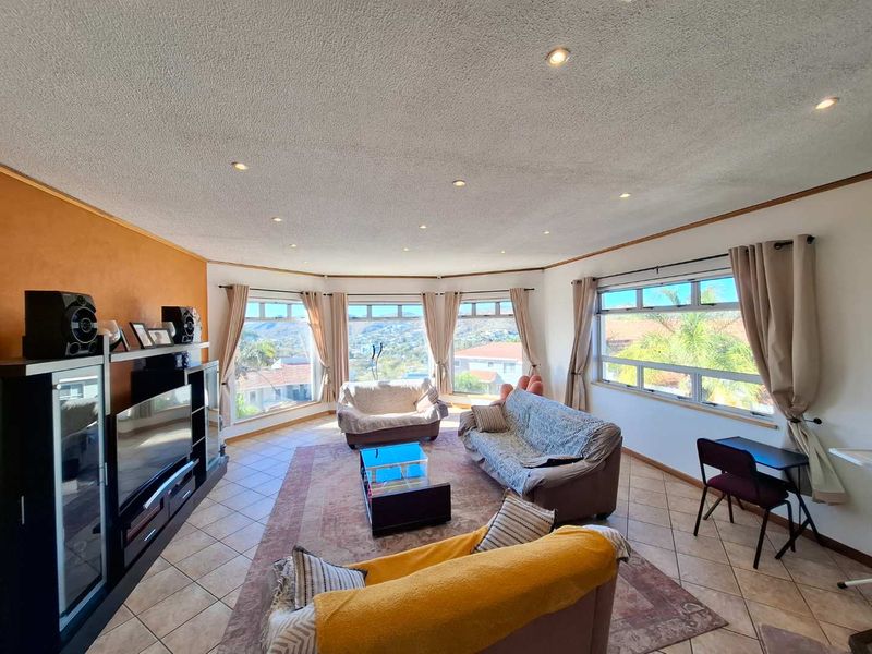 Spacious living room featuring large bay windows with scenic views, tiled flooring, and recessed downlighting, offering a bright and open atmosphere.