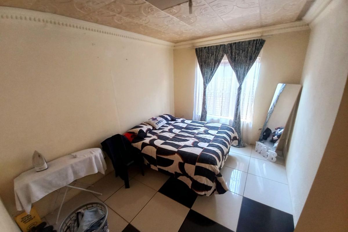 A bedroom featuring a patterned ceiling, tiled flooring, and a window with curtains, providing a basic living space.