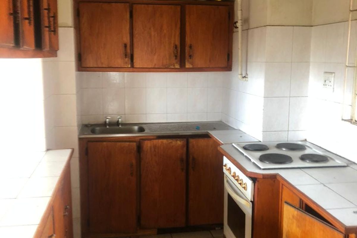 A dated kitchen featuring wooden cabinetry, tiled countertops, and built-in cooking appliances, offering significant potential for modernization and renovation.