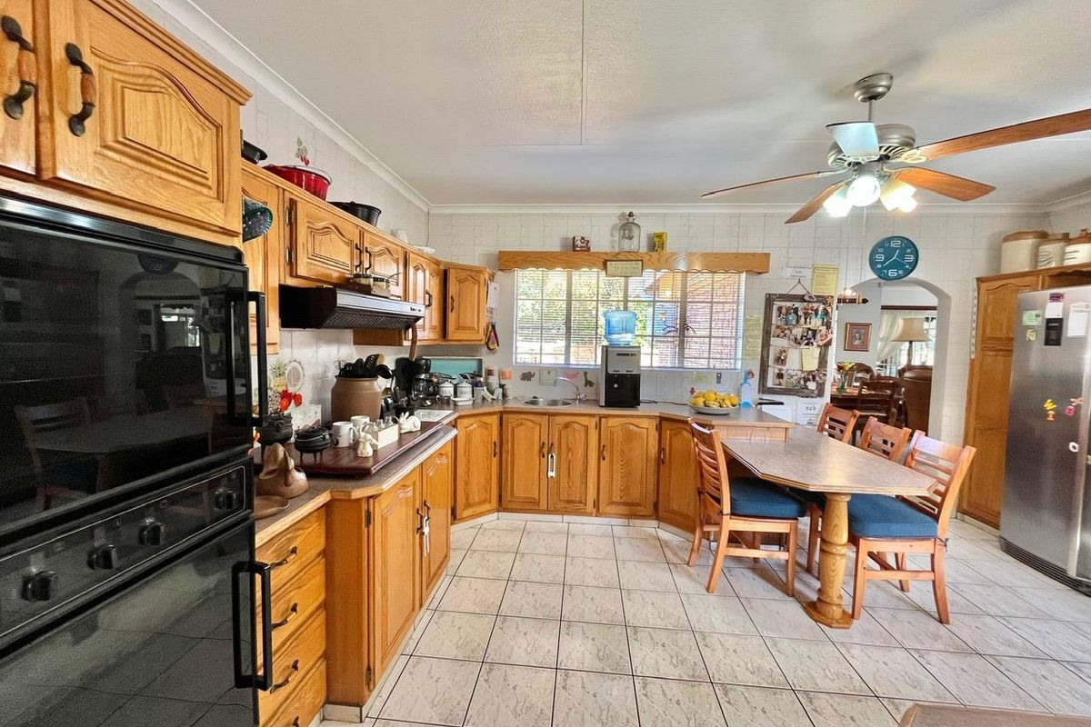Spacious kitchen featuring traditional timber cabinetry, tiled flooring, built-in oven, and an integrated dining area with a ceiling fan.