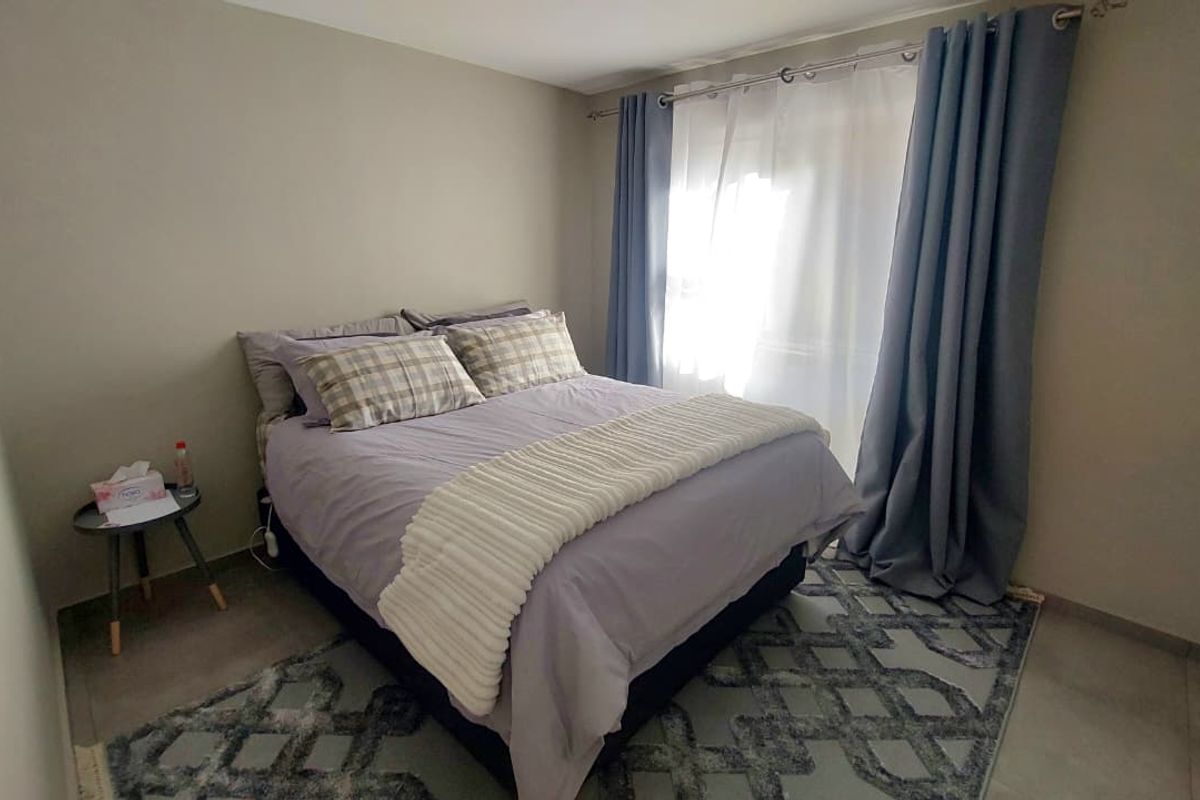 A functional bedroom featuring neutral wall tones and tiled flooring, with natural light entering through a window dressed with curtains.