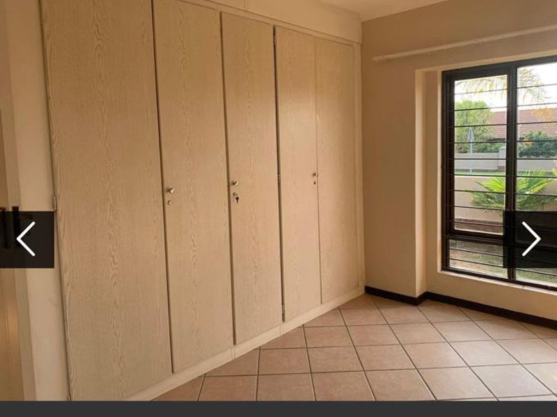 A clean, empty bedroom featuring neutral tiled flooring and extensive built-in cupboard storage with natural light from a window fitted with security bars.