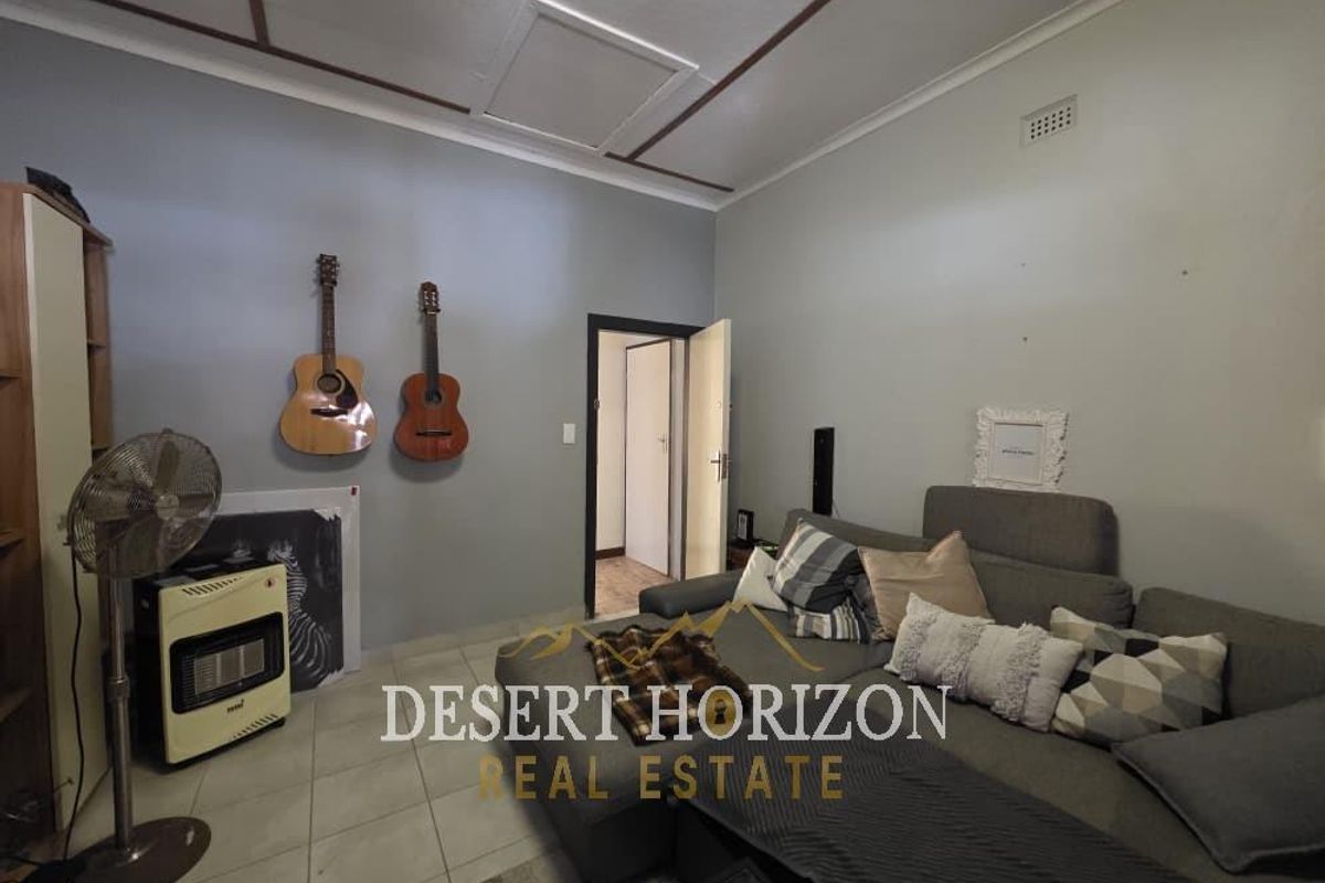 A living room featuring tiled flooring, a ceiling with decorative trim, and a doorway leading to an adjacent hallway.