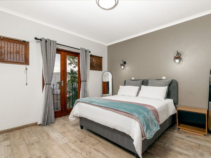 A well-maintained bedroom featuring timber-look flooring, a feature wall, wall-mounted lighting, and direct access to a private balcony through timber french doors.