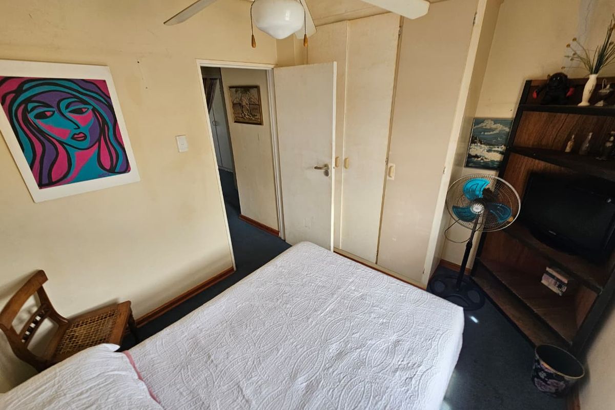 A bedroom featuring built-in cupboards, a ceiling fan, and carpeted flooring, offering a functional layout with potential for cosmetic updates.
