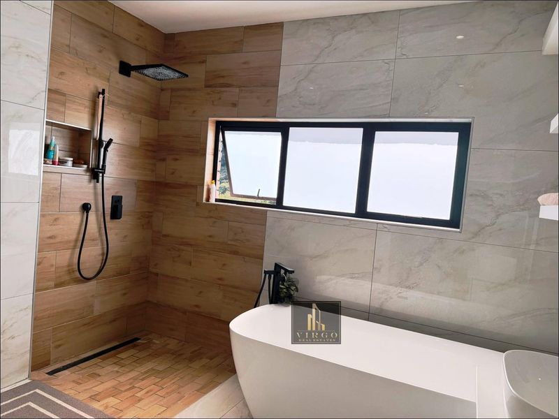 Modern bathroom featuring a sleek freestanding bathtub, a spacious walk-in shower with a rain shower head, and contemporary black fixtures.