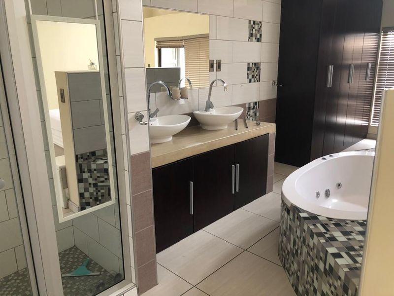 Modern bathroom featuring a double vanity with vessel sinks, built-in cabinetry, a jetted bathtub with mosaic tiling, and a separate shower enclosure.
