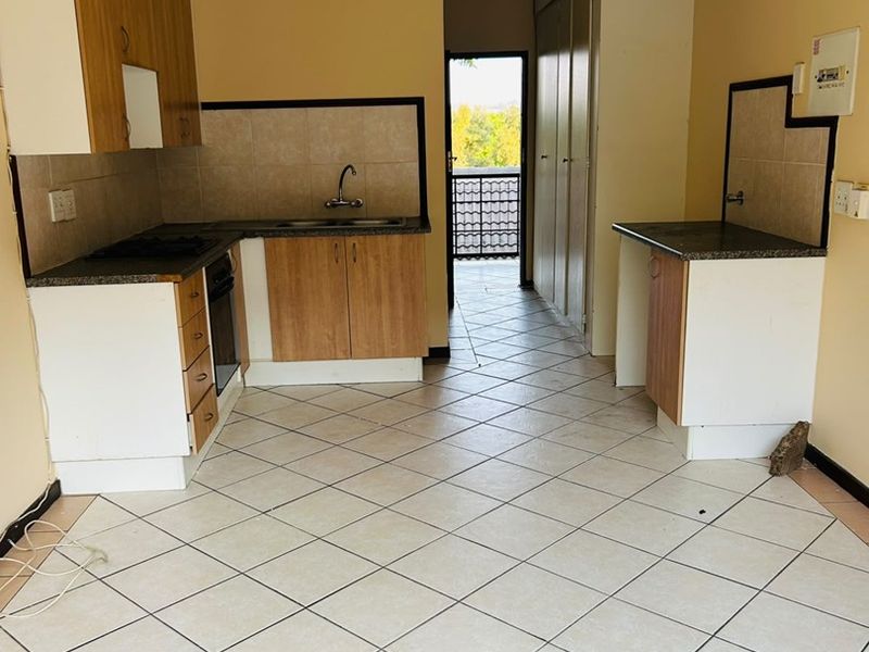 A dated kitchen featuring laminate cabinetry, granite countertops, built-in oven, and tiled flooring, leading to a balcony area.