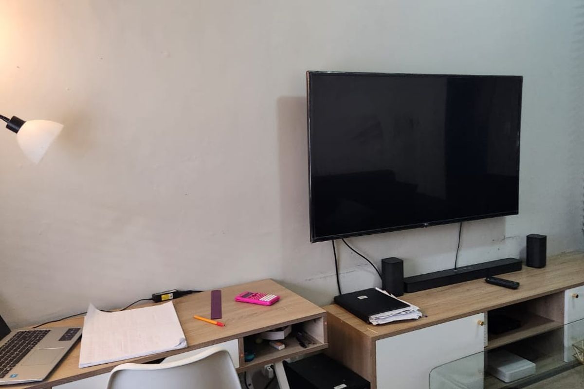 A living room area featuring tiled flooring and a wall-mounted television, showing signs of wear on the walls requiring maintenance.