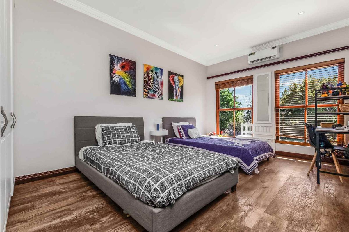 A well-maintained bedroom featuring timber-look flooring, built-in wardrobes, and a split-system air conditioner, with large windows providing natural light.