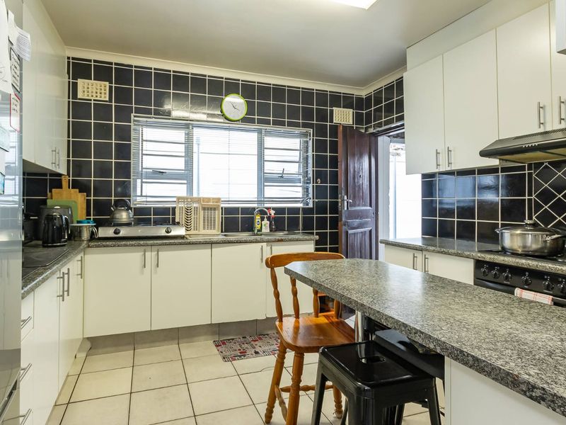 A functional kitchen featuring white cabinetry, granite countertops, a black tiled backsplash, and built-in cooking appliances with tiled flooring.