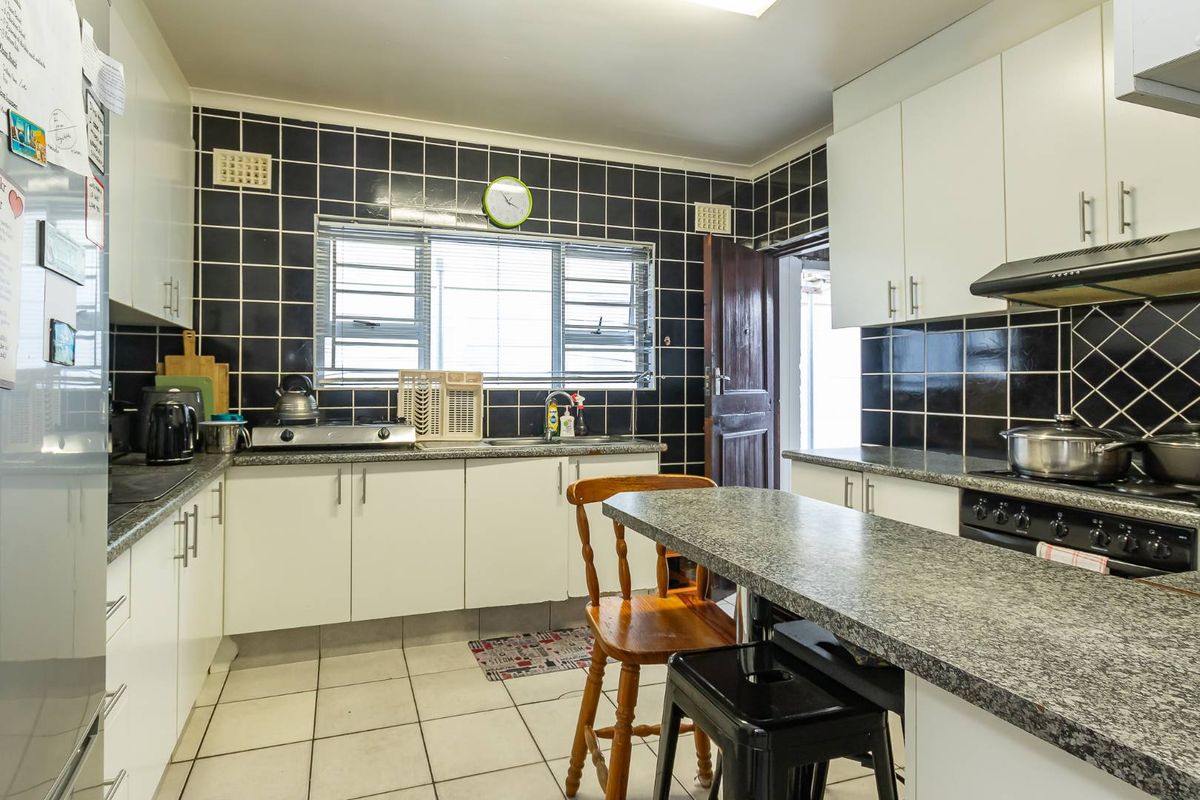 A functional kitchen featuring white cabinetry, granite countertops, a black tiled backsplash, and built-in cooking appliances with tiled flooring.