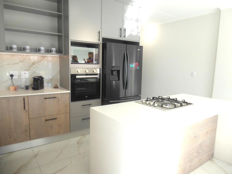 Modern kitchen featuring sleek grey and wood-tone cabinetry, stone countertops, a central island with a gas cooktop, and high-end built-in appliances.