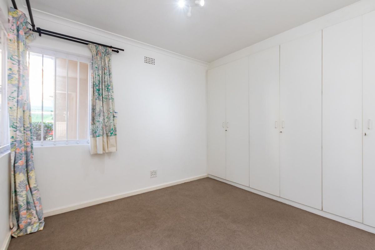 A clean, empty bedroom featuring neutral carpeting and a large wall of built-in white cabinetry for storage.