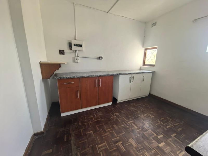 A functional scullery or utility area featuring parquet flooring, built-in cabinetry with laminate countertops, and a small leaded glass window.